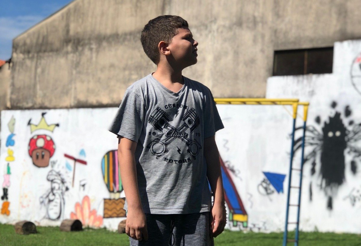 Menino observa o horizonte em frente a um muro grafitado, em Americana.